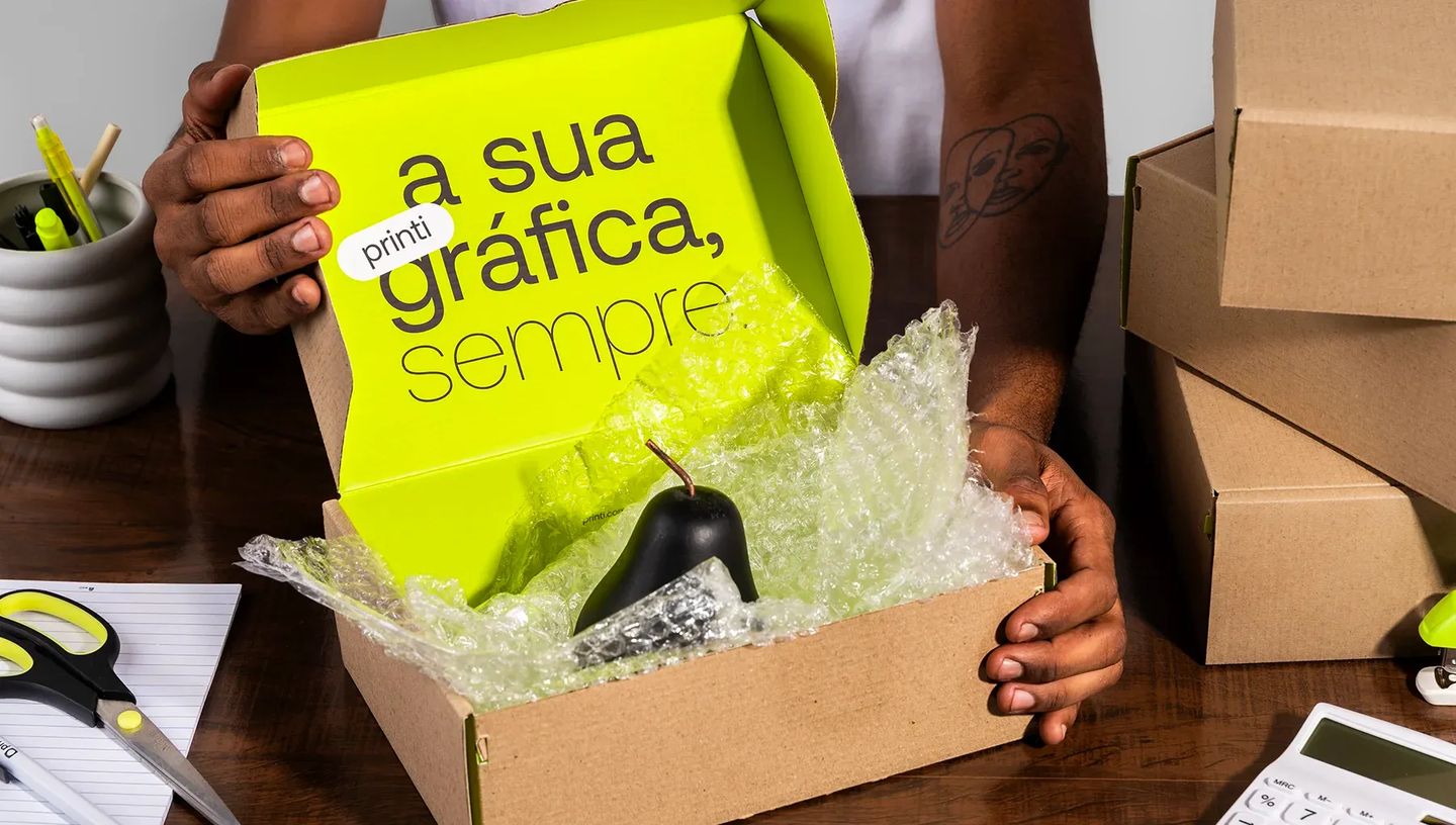 Pessoa embalando produto com plástico bolha em caixa de transporte personalizada Printi, demonstrando segurança e branding no envio.