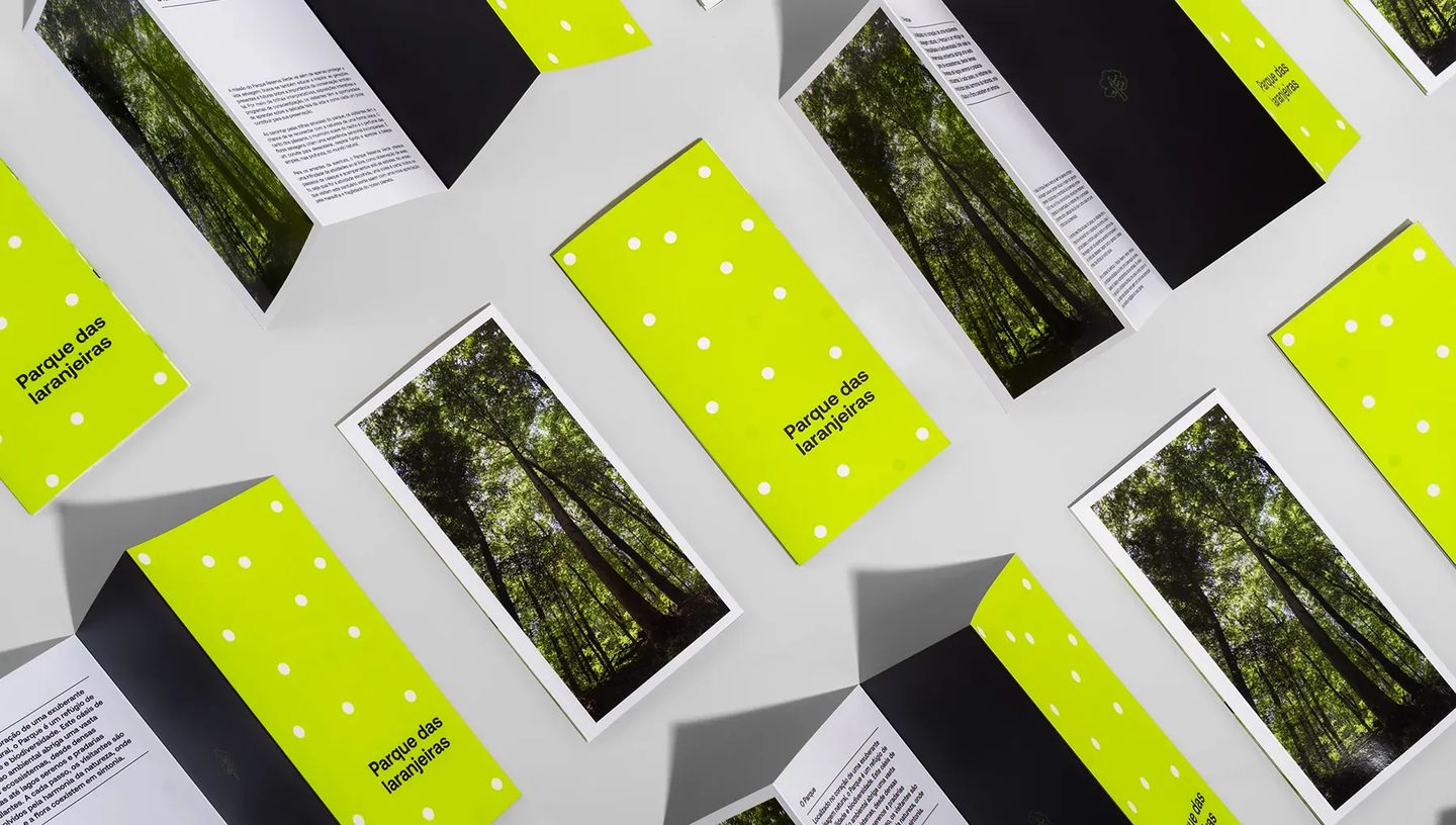 Composição de folders personalizados com 3 dobras da Printi espalhados em fundo cinza, exibindo design institucional e qualidade de impressão premium.