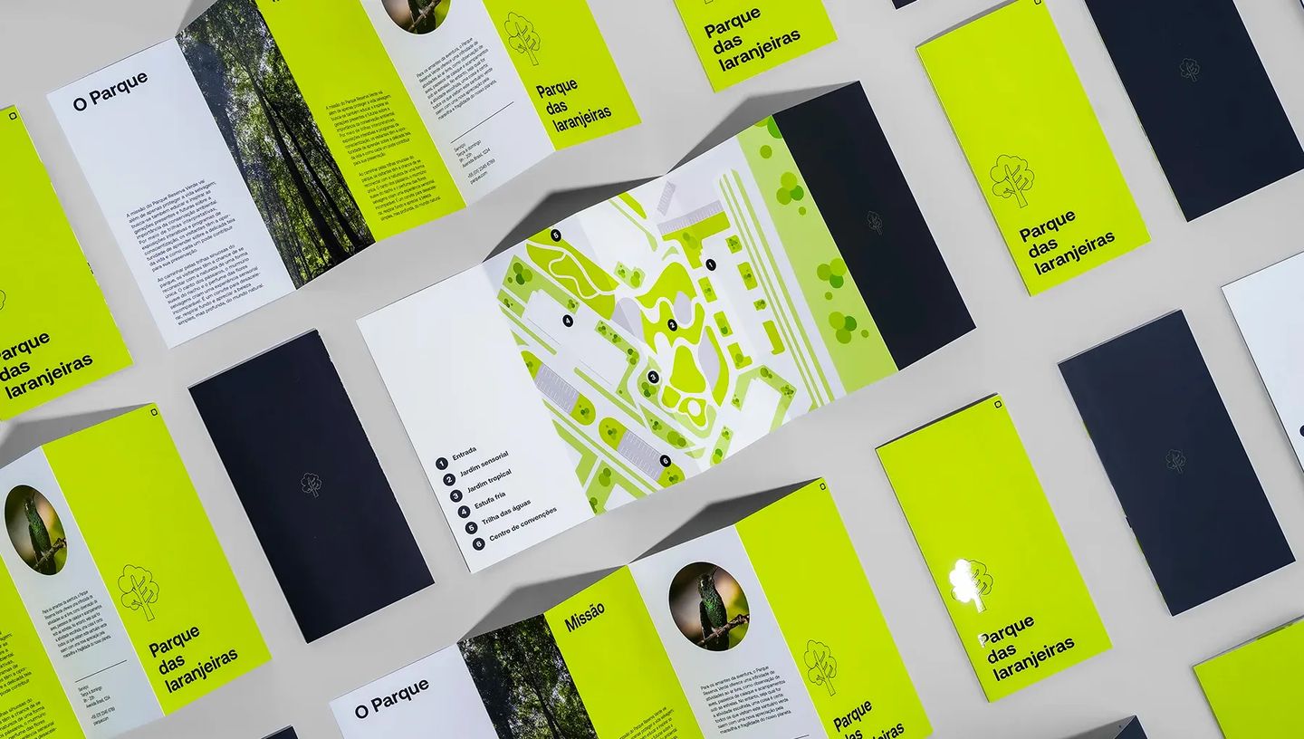 Mockup com várias unidades de folder 4 dobras em diferentes posições. Em destaque no centro, o folder aberto revela um mapa ilustrado com legenda dos pontos turísticos, demonstrando a paginação e o layout do material impresso.