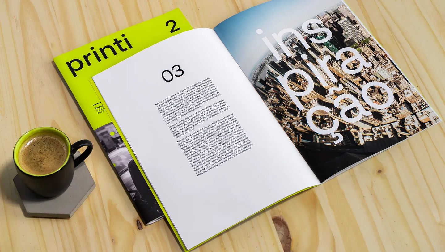 Revista personalizada aberta em mesa de madeira ao lado de xícara de café, mostrando conteúdo editorial com fotografia urbana e tipografia nítida.