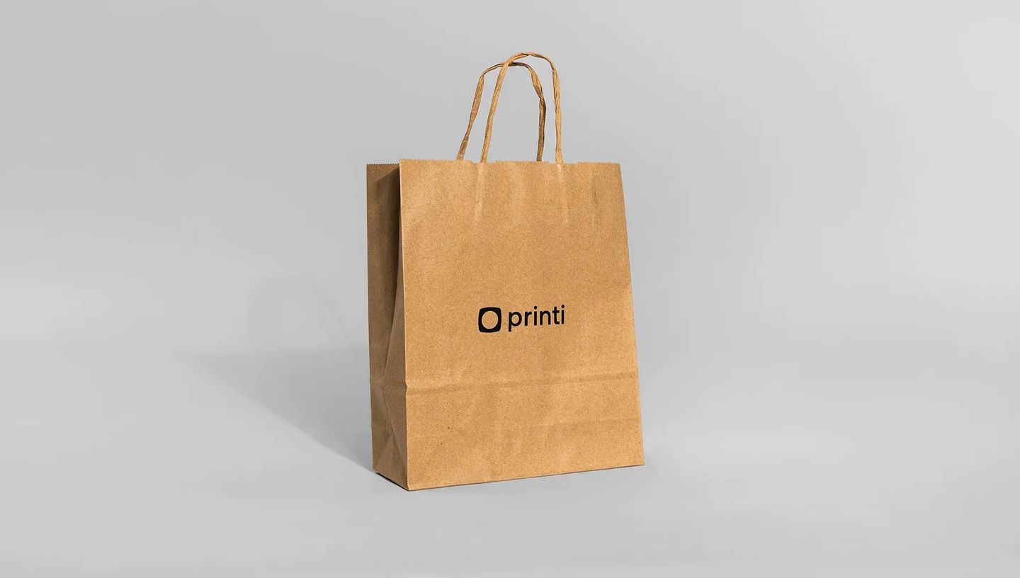 Sacola de papel personalizada com alça torcida em fundo cinza neutro. Modelo de sacola kraft para comércio e presentes com o logo da Printi estampado no centro.