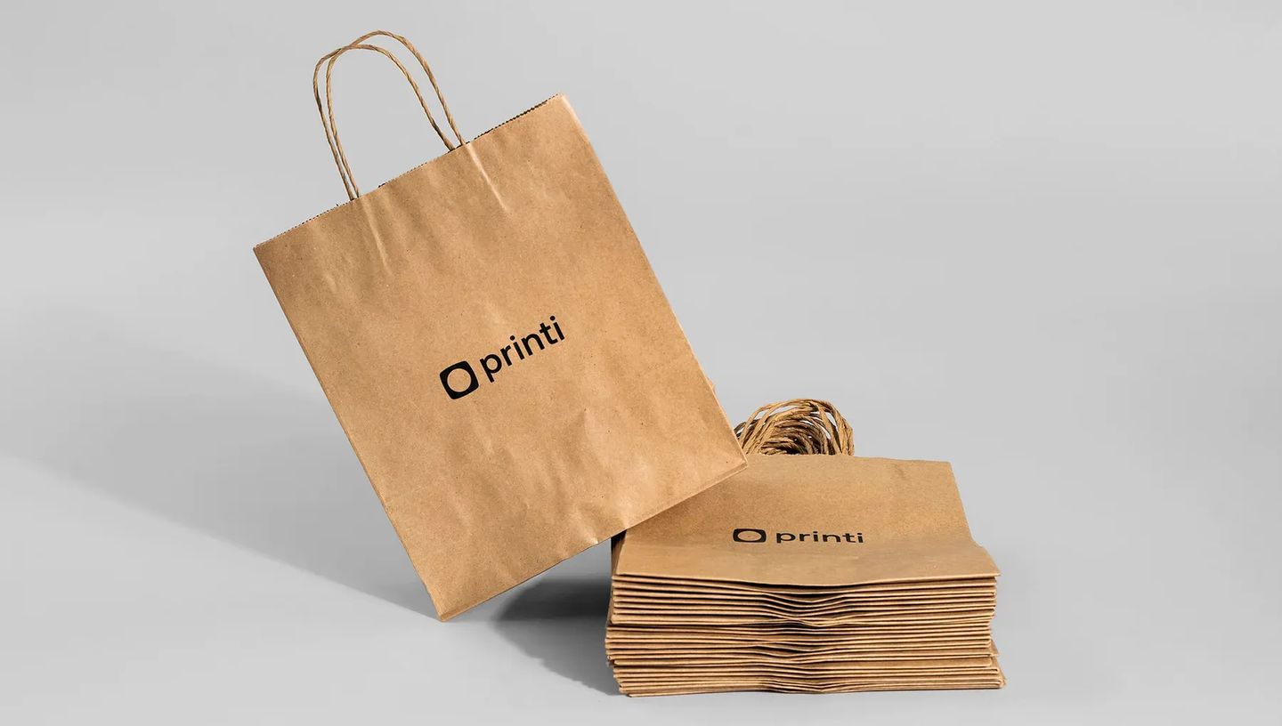 Pilha de sacolas de papel kraft personalizadas com uma unidade em destaque de pé. Embalagens sustentáveis e personalizadas para marcas e lojas em geral.