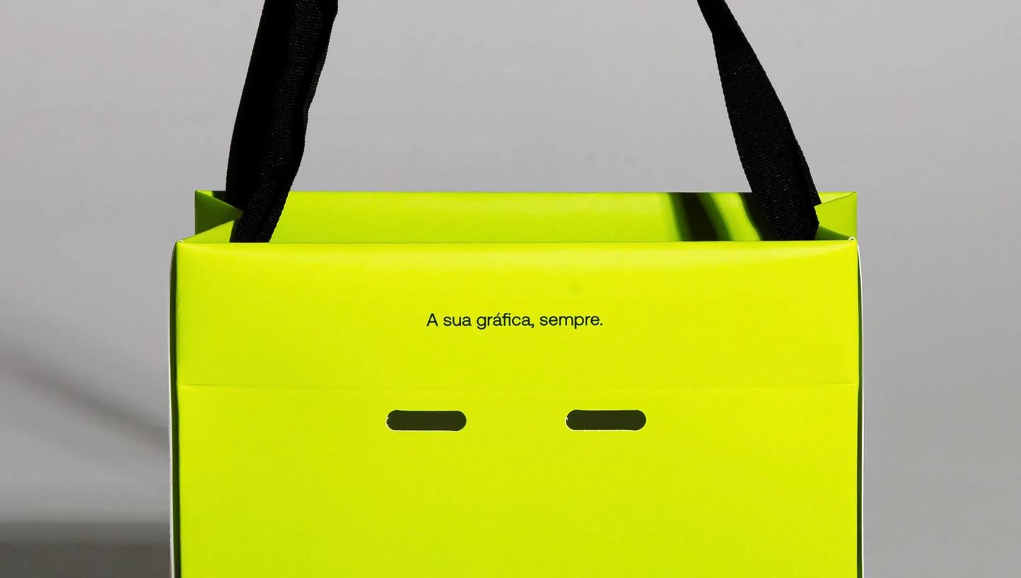 Detalhe superior de sacola de papel teepee personalizada na cor verde neon com frase institucional e alças de gorgurão pretas resistentes.