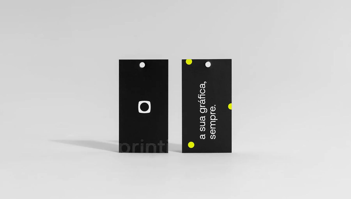 Par de Tag Econômica em papel cartão preto com acabamento fosco e frase "a sua gráfica, sempre" impressa em branco com detalhes em amarelo neon.