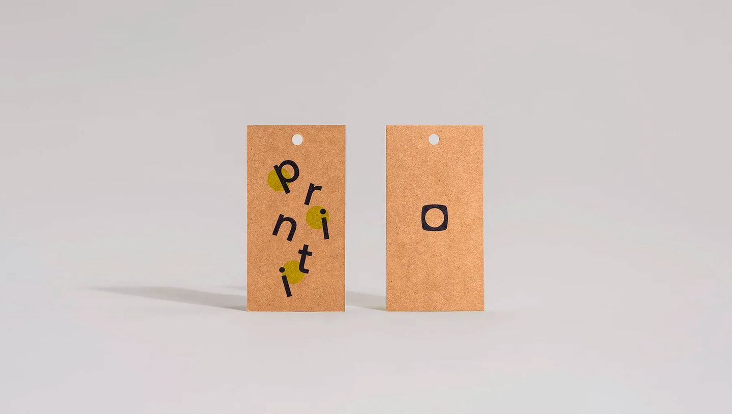Detalhe frontal e verso de tags personalizadas em papel kraft com logotipo da Printi, exibindo qualidade de furação e textura do material.