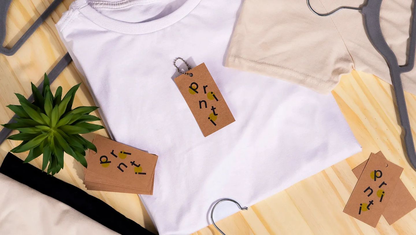 Tag personalizada em papel kraft aplicada a uma camiseta branca em cenário de e-commerce de moda, destacando o uso do produto como etiqueta de marca.