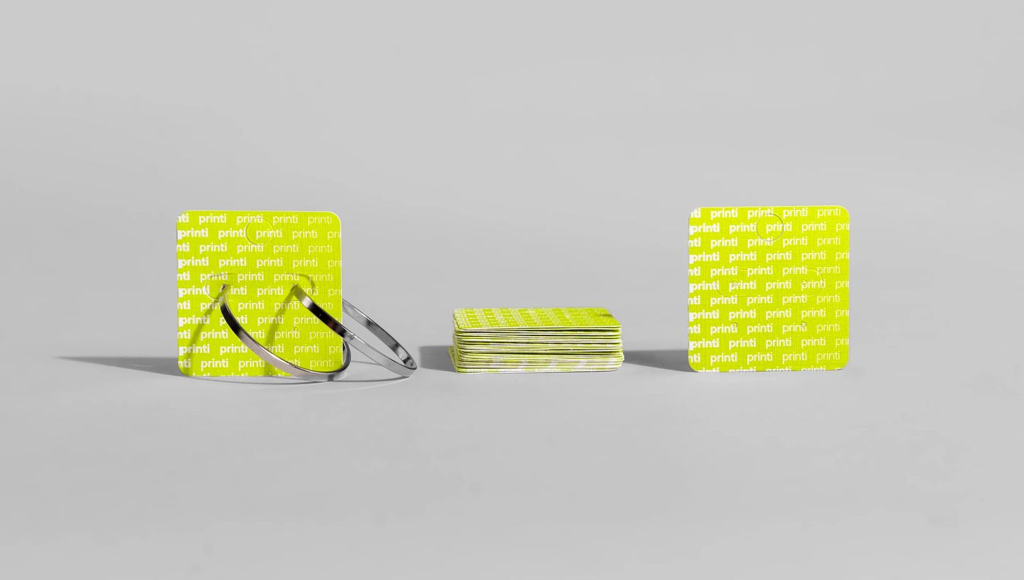 Três cartelas para bijuteria personalizadas da Printi exibidas em fundo neutro, com brincos de argola fixados para demonstração de uso