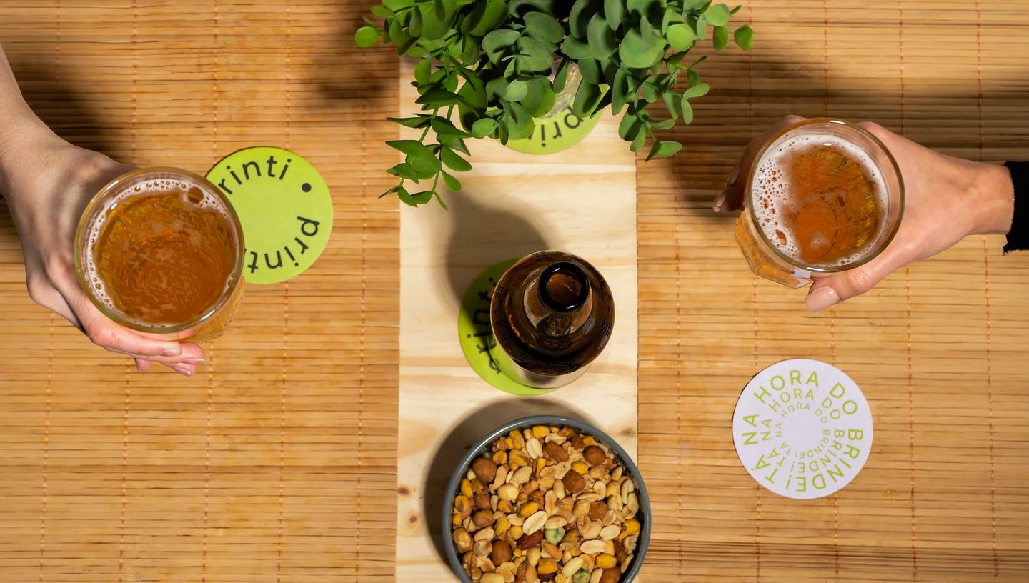 Vista superior de mesa com copos de cerveja apoiados em bolachas de chopp de papelão personalizadas.