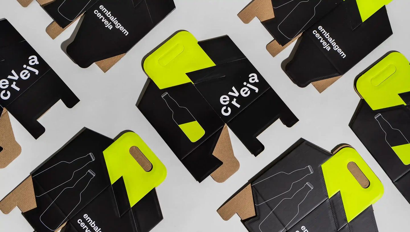 Embalagens para cerveja em papel cartão preto com detalhes em verde neon, dispostas abertas sobre fundo neutro. As caixas apresentam recorte para alça, ilustração minimalista de garrafa e a inscrição “embalagem cerveja”