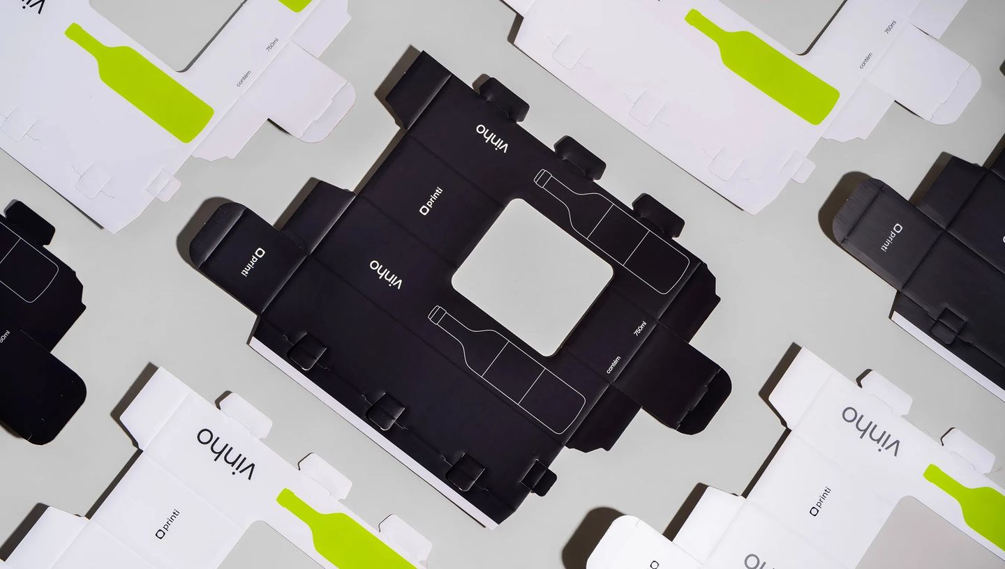 Embalagens personalizadas para vinho abertas e planificadas com design em preto e branco e detalhes verdes da Printi, mostrando estrutura de caixa para garrafa usada em presentes, eventos e vendas.