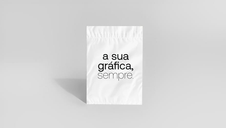 Envelope de segurança plástico branco com fechamento selado, exibindo a frase “a sua gráfica, sempre.” impressa em preto no centro. O envelope aparece em pé sobre fundo neutro