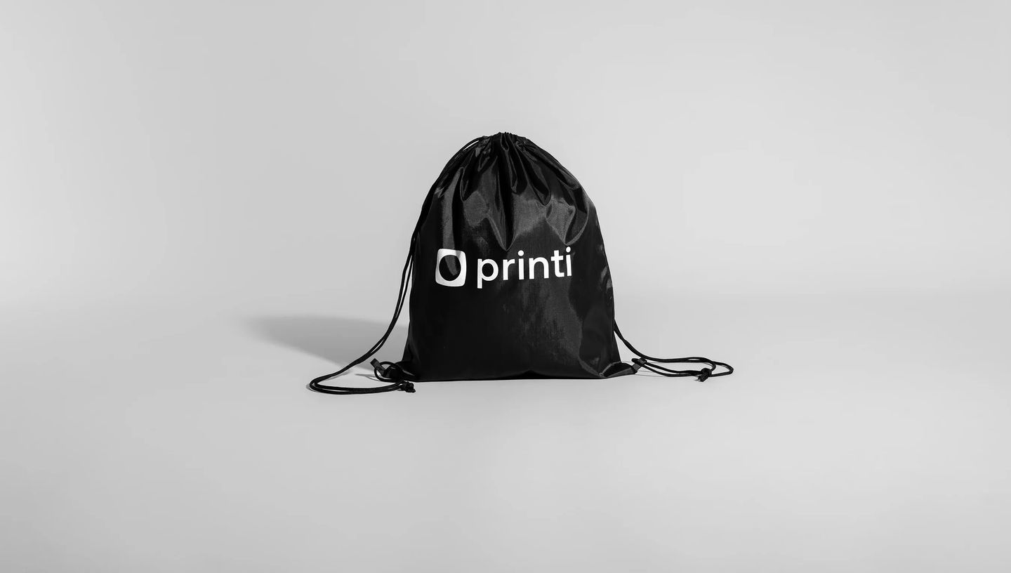 Mochila saco preta personalizada com logo branco da Printi, exibida em fundo branco e neutro.