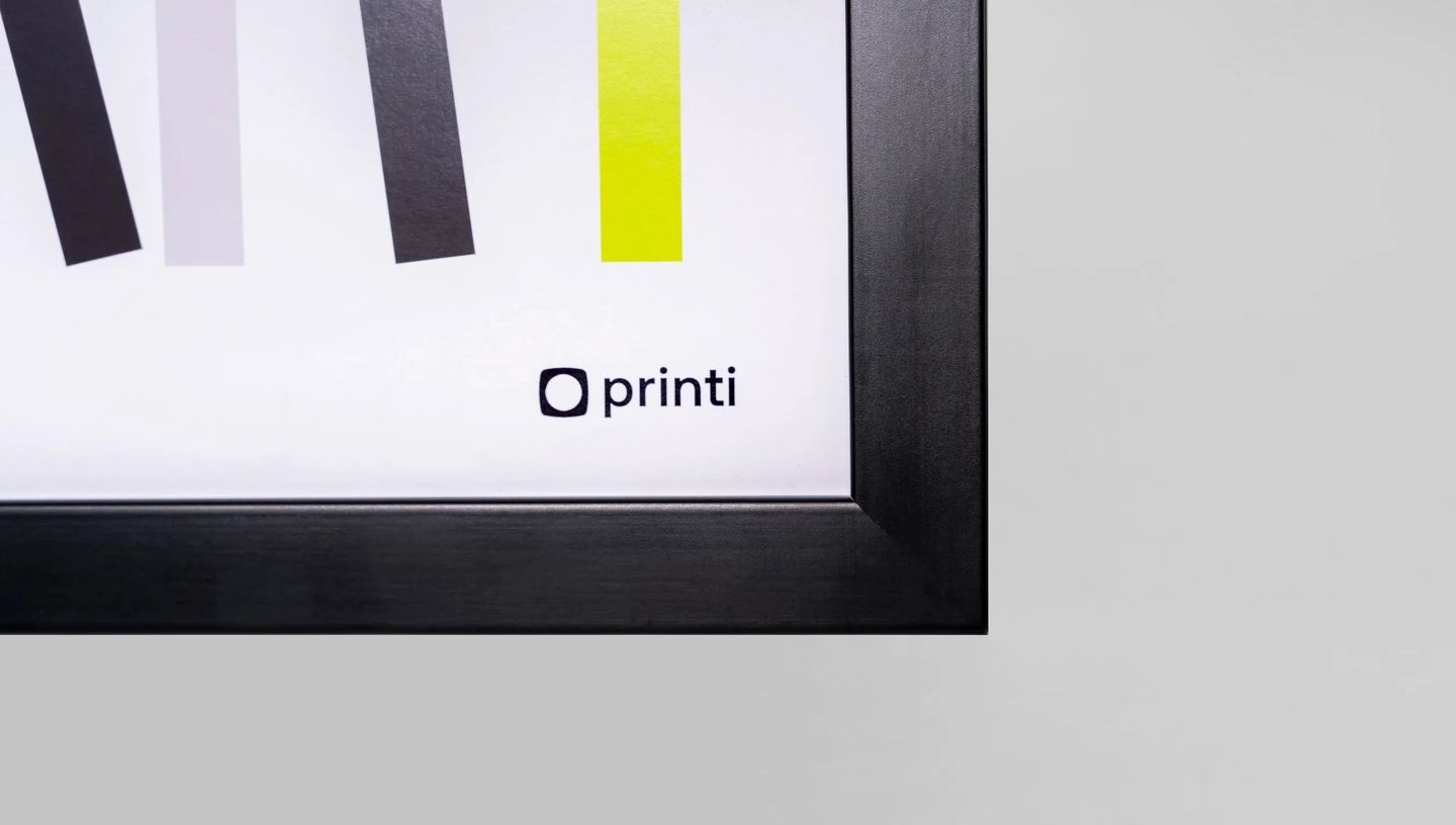 Detalhe de canto de quadro personalizado com moldura preta e logotipo Printi em fundo branco.