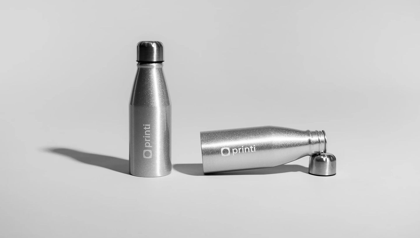 Squeeze metálico personalizado com acabamento prateado e tampa de inox, com logo Printi, exibido em duas posições sobre fundo neutro para destacar o design e a personalização do produto.