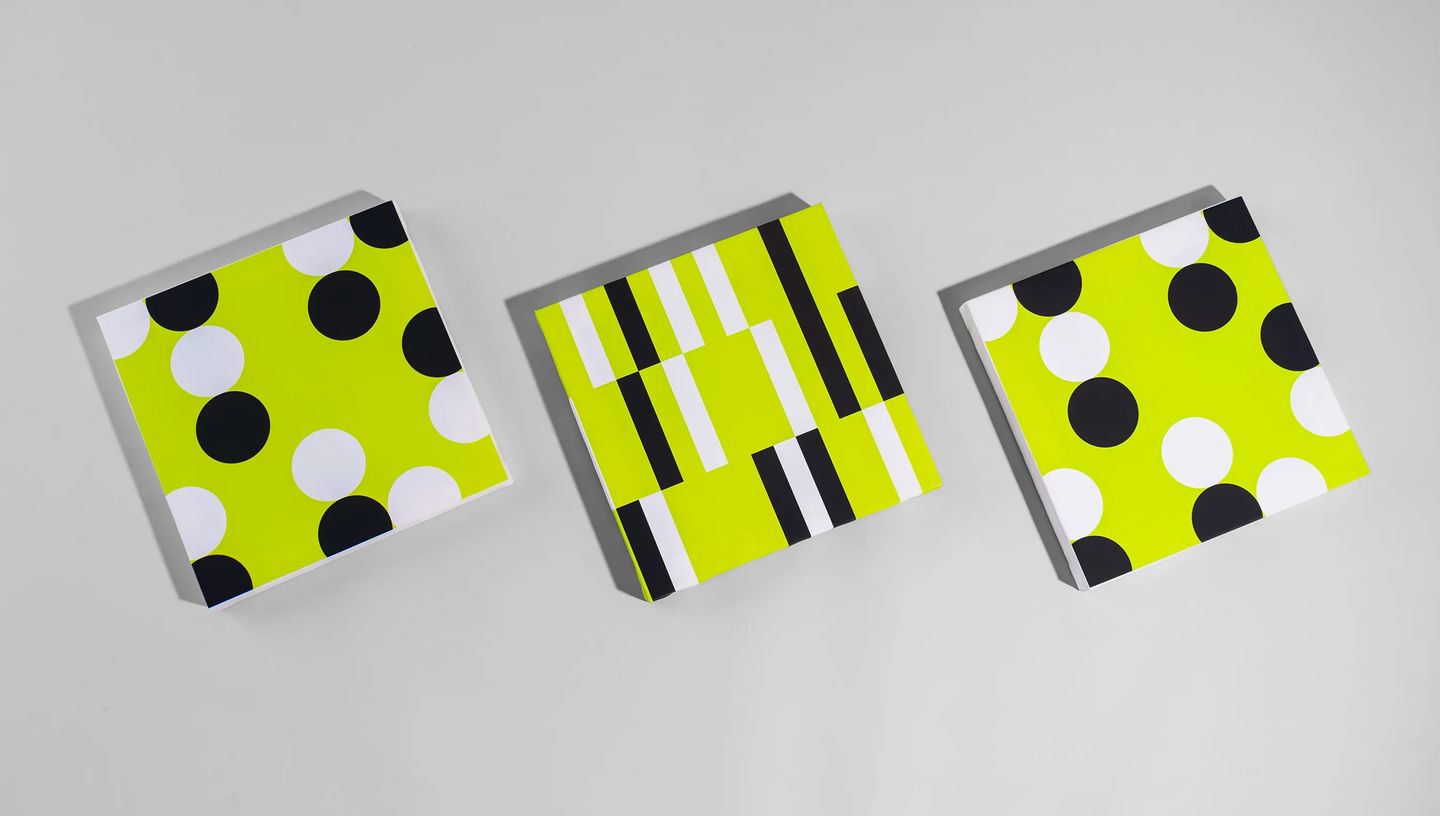 Três telas decorativas todas em formato quadrado com estampas de bolinhas e listras em preto, branco e verde-limão, posicionadas lado a lado sobre fundo cinza.