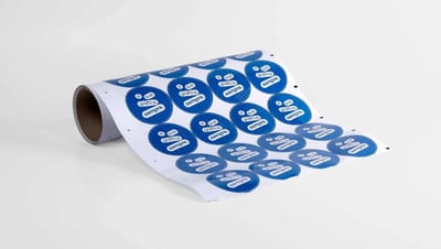 Rolo de adesivos redondos personalizados com impressão em azul e branco, contendo a frase “a sua gráfica, sempre”, utilizados para rotulagem de produtos, embalagens, brindes e identificação de marca em negócios e lojas.