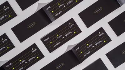 Várias capas de carnê pretas com detalhes gráficos em verde neon dispostas em padrão repetido sobre fundo cinza, com a frase “carnê, a sua gráfica, sempre.” estampada.