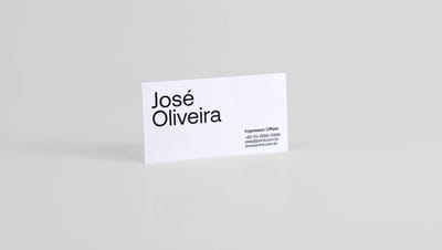 Cartão de visita profissional em papel branco com design minimalista em preto, exibindo o nome “José Oliveira” e informações de contato, apresentado em estúdio sobre fundo neutro para destacar o layout limpo e tipografia moderna do material impresso.