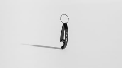 Chaveiro Abridor Clane preto em posição vertical, com anel metálico e logo da Printi,