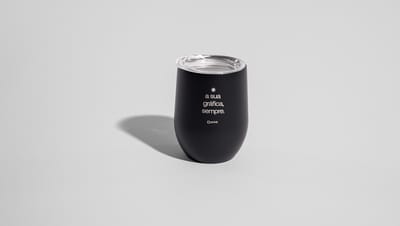 Copo Térmico de 400 ml preto com tampa, apoiadao em superfície lisa e branca, com logo e frase personalizada dizendo "a sua gráfica sempre"