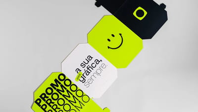 Molde de cubo personalizado em papelão aberto sobre uma superfície branca e lisa, com layout colorido em branco, preto e verde, incluindo textos promocionais dizendo "promo" e "printi, a sua gráfica, sempre; smile e logotipo da Printi, pronto para montage