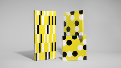 Três modelos de banner com moldura em painel rígido expostos em pé sobre fundo cinza. À esquerda, o banner apresenta uma estampa geométrica com listras verticais em preto, branco e amarelo vibrante, criando um efeito visual moderno e dinâmico. À direita, 
