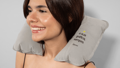 Mulher sorridente usando almofada de pescoço inflável personalizada da Printi, com estampa em preto e amarelo sobre material cinza