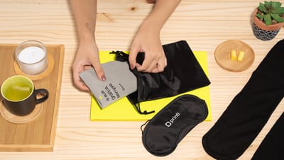 Pessoa colocando lenço dentro de bolsa do kit de viagem ao lado de máscara para dormir e itens de decoração