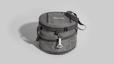Bolsa térmica flexível redonda na cor cinza mescla, com alça de ombro ajustável e abridor de garrafa branco acoplado.