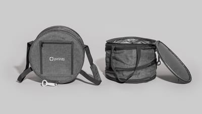 Bolsa térmica flexível redonda na cor cinza mescla, com alça de ombro ajustável e abridor de garrafa branco acoplado.
