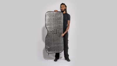 Pessoa segurando um protetor solar prateado para carro, com textura refletiva e formato curvado, ideal para cobrir o para-brisa.