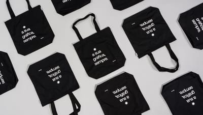 Com certeza! As sacolas de algodão reciclado (ou ecobags) são muito populares. Aqui estão as opções de alt text para SEO para as duas imagens.  Imagem 1 (Com a modelo) Opção 1 (Curta e Direta): Mulher segurando uma ecobag preta de algodão reciclado com a 