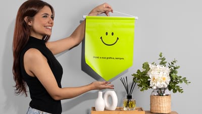 Pessoa segurando Flâmula personalizada na cor verde com smile e slogan da Printi, perto de vasos e planta
