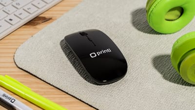 Mouse sem fio personalizado na cor preta com logo da Printi sobre mouse pad, ao lado de fone de ouvido verde.