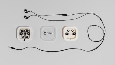 Fone de ouvido com microfone personalizado com logo da Printi na capa, com todos os acessórios ao redor.