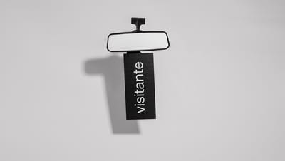 Display Retrovisor preto com a palavra "visitante" pendurado no espelho retrovisor interno de um carro