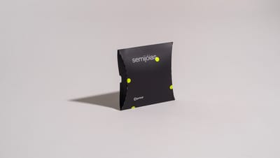Embalagem almofada bijuteria preta com design moderno e logo Printi, em fundo cinza neutro