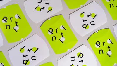Embalagens tipo almofada personalizadas em papel cartão nas cores branco e verde neon com a marca Printi impressa em preto, dispostas em padrão repetido sobre fundo neutro
