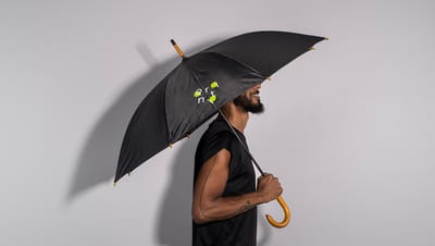 Homem negro de barba usando uma blusa de manga preta, segurando guarda-chuva preto com cabo de madeira e estampa personalizada da Printi