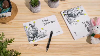 Cartão de Páscoa personalizado com ilustração de coelho e elementos de decoração temática sobre mesa de madeira.