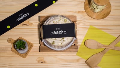 Cinta para bolo personalizada envolvendo embalagem de plástico com bolo caseiro, em composição com utensílios de cozinha e decoração de mesa