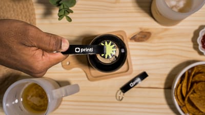 Pessoa utilizando um Chaveiro Abridor Clane personalizado da Printi, em cima de uma mesa de madeira e com canecas ao redor