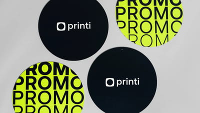 Conjunto de placas circulares personalizadas com design moderno da Printi, em fundo preto com logotipo branco e versões em verde-limão com tipografia “PROMO”, utilizadas como materiais de comunicação visual e sinalização promocional para eventos, campanha