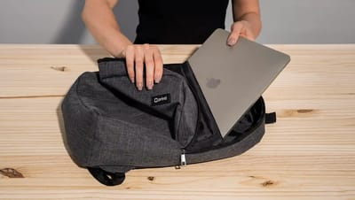 Mochila personalizada para notebook da Printi aberta sobre mesa de madeira enquanto uma pessoa coloca um laptop dentro do compartimento