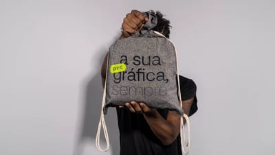 Pessoa segurando mochila saco personalizada em algodão reciclado cinza com estampa “a sua gráfica, sempre.” da Printi