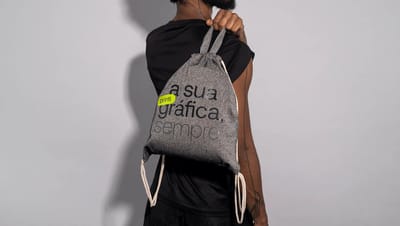 Homem usando mochila saco personalizada em algodão reciclado cinza com estampa “a sua gráfica, sempre.” da Printi