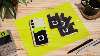 Porta Cartões para Celular em Silicone aplicado na traseira de um smartphone em ambiente de escritório, ao lado de itens de papelaria e café