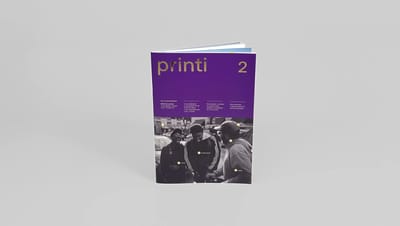 Revista personalizada com capa roxa e detalhes em dourado, aberta em pé sobre fundo neutro.