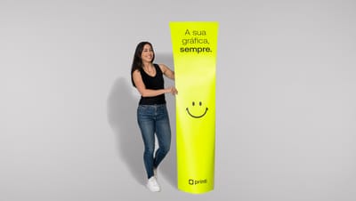 Mulher branca de cabelos lisos com regata preta, calça jeans skinny e tênis branco segurando totem banana com smile na cor verde-limão com fundo cinza