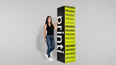 Mulher branca de cabelos lisos com regata preta, calça jeans skinny e tênis branco segurando totem quadriedro nas cores preto e verde-limão